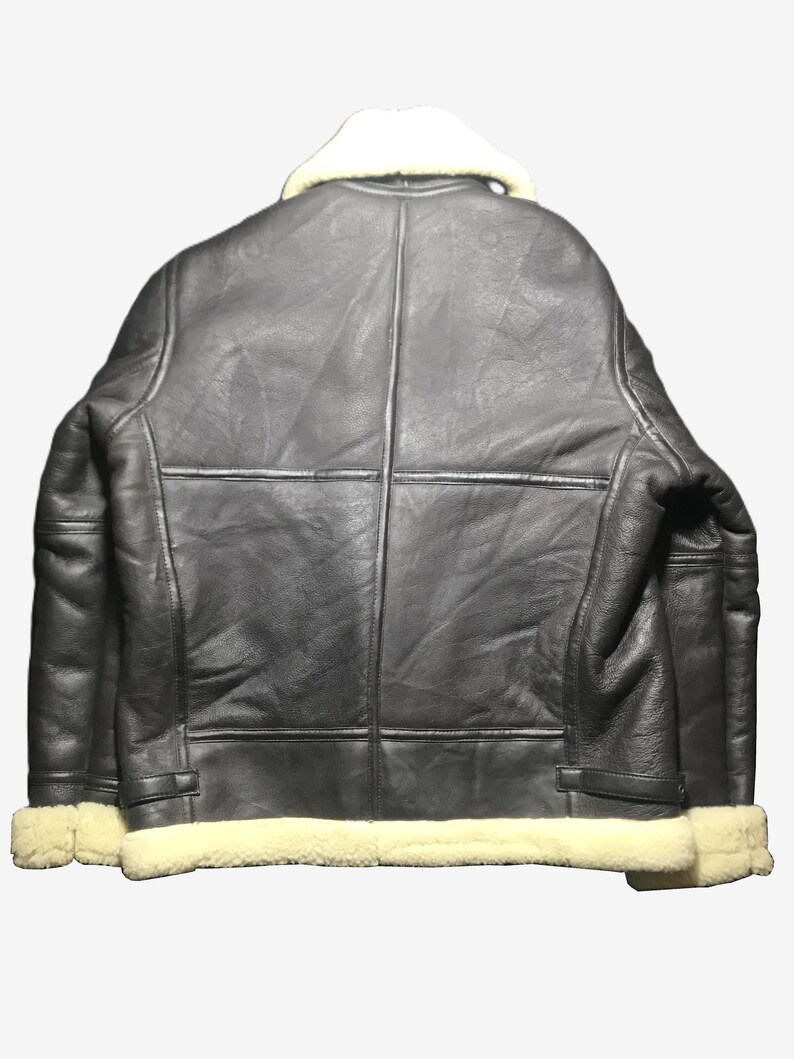May include: A black leather jacket with a cream-colored shearling collar and trim. The jacket has a classic design with visible stitching and paneling. The back view showcases the jacket's structure and details.