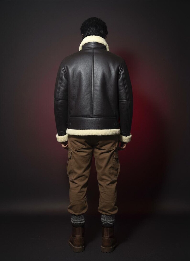 May include: A black leather jacket with a cream-colored shearling collar and trim. The jacket is worn with brown cargo pants and brown boots. The person is facing away from the camera against a dark background.