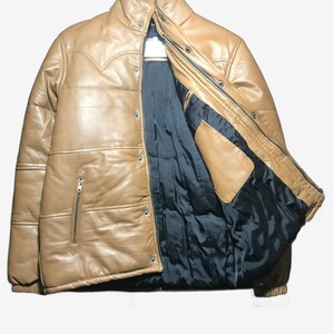 K&ouml;nnte beinhalten: Hellbraune Lederjacke mit Steppdesign und schwarzem Innenfutter. Die Jacke hat einen Rei&szlig;verschluss, Druckkn&ouml;pfe und einen hohen Kragen. Die Jacke hat einen Western-Stil Joch Detail.
