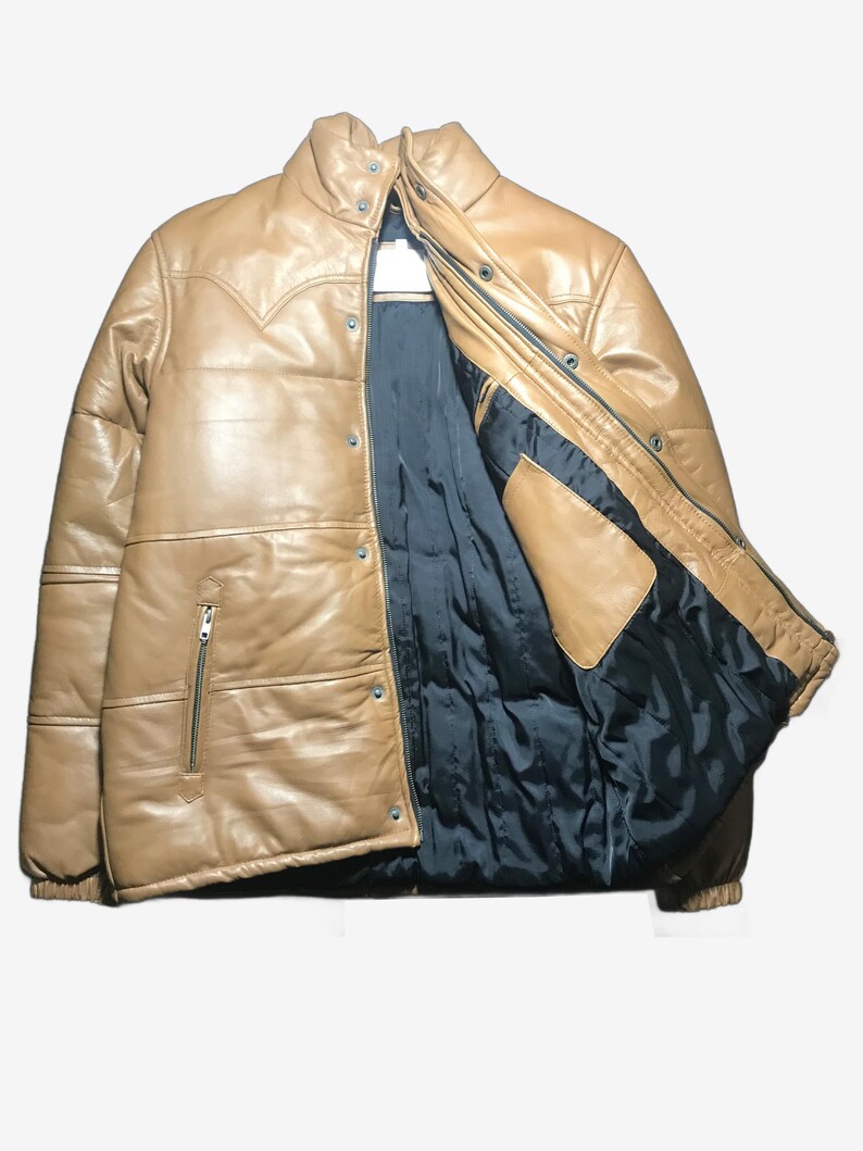 K&ouml;nnte beinhalten: Hellbraune Lederjacke mit Steppdesign und schwarzem Innenfutter. Die Jacke hat einen Rei&szlig;verschluss, Druckkn&ouml;pfe und einen hohen Kragen. Die Jacke hat einen Western-Stil Joch Detail.