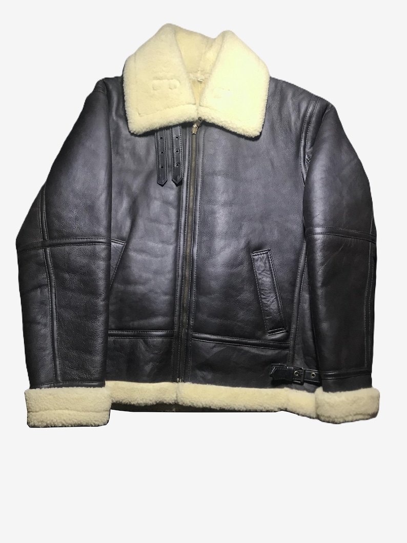 May include: A dark brown leather jacket with a cream-colored shearling collar and lining. The jacket features a front zipper, two front pockets, and a buckle at the waist. The cuffs are also lined with cream-colored shearling.