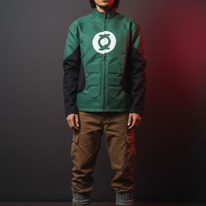 May include: Green and black jacket with a white circular emblem on the chest. The jacket has a zip-up front and padded details. The person is wearing brown cargo pants, gray socks, and brown boots. The jacket is a costume.