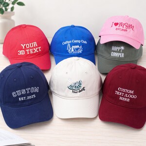 Könnte beinhalten: Eine Sammlung von sechs Baseballkappen in verschiedenen Farben, darunter Rot, Blau, Pink, Dunkelgrau, Marineblau, Weiß und Kastanienbraun. Jede Kappe zeigt einzigartige gestickte Texte oder Grafiken wie 'YOUR 3D TEXT', 'Cultus Camp Club', 'I MOM EST.2025', 'HAPP CAMPER', 'CUSTOM EST.2025', 'Your design' und 'CUSTOM TEXT /LOGO HERE'.
