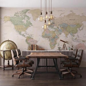 Könnte beinhalten: Ein Esszimmer mit einem großen Holztisch und Lederstühlen. Die Wand ist mit einer Weltkarte tapeziert. Ein Globus und Bücher sind zu sehen. Hängelampen mit freiliegenden Glühbirnen beleuchten den Raum.