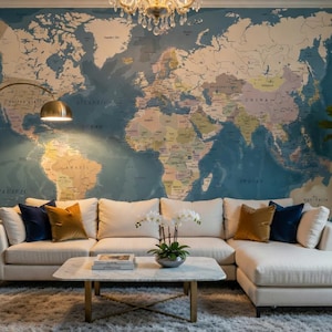 Peut inclure: Une grande fresque murale représentant une carte du monde détaillée dans des tons de bleu, beige et vert. Un canapé d'angle blanc avec des coussins bleu marine et dorés est placé devant le mur. Une table basse en marbre porte des livres et une orchidée.