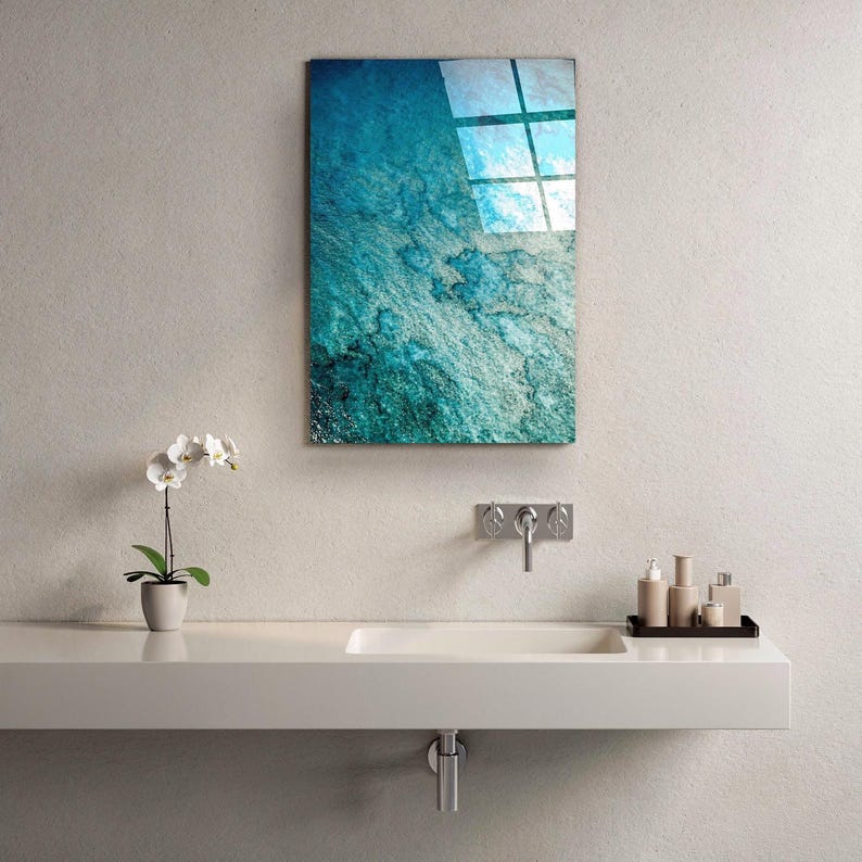 Puede incluir: Una pieza de arte mural rectangular con un dise&ntilde;o abstracto texturizado, turquesa y azul, cuelga sobre un lavabo blanco. Tambi&eacute;n se ven una peque&ntilde;a orqu&iacute;dea en maceta y art&iacute;culos de tocador.