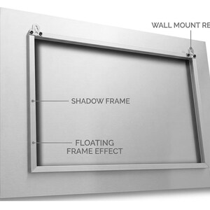 Puede incluir: Un marco de metal plateado con un marco de sombra y un efecto de marco flotante. Las palabras "WALL MOUNT READY" son visibles, junto con el texto "SHADOW FRAME" y "FLOATING FRAME EFFECT". El marco tiene herrajes para montaje en pared.