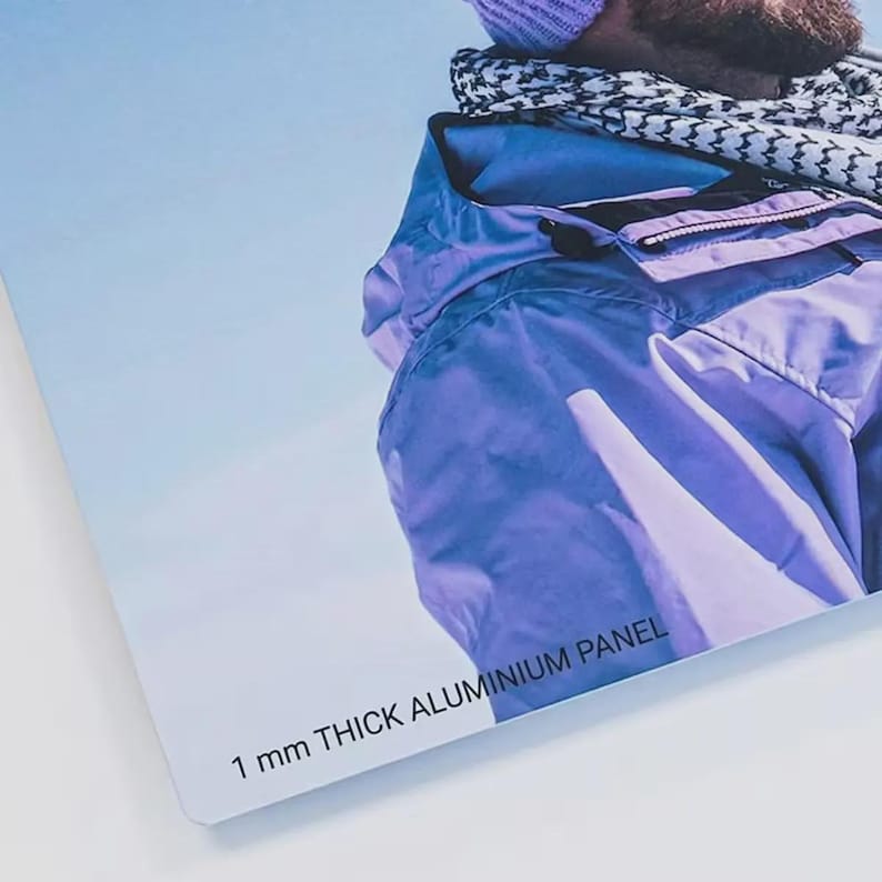 May include: A rectangular aluminum panel featuring a printed image of a person wearing a purple jacket, a purple beanie, and a black and white patterned scarf. The text 1 MM THICK ALUMINIUM PANEL is printed in black on the lower left corner of the surface.