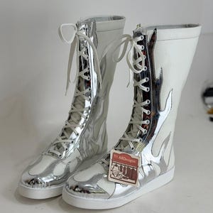 Puede incluir: Un par de botas altas blancas y plateadas con un dise&ntilde;o de llamas. Las botas tienen cordones blancos y una suela blanca. Las botas tienen una etiqueta que dice "ARDesigns".