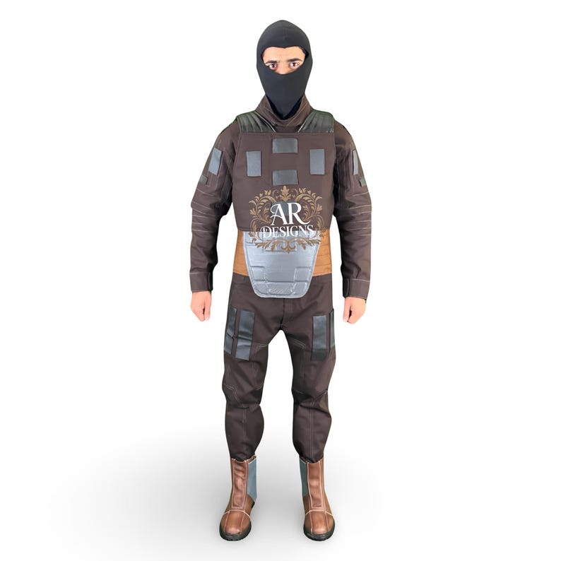May include: A brown tactical suit with a black balaclava, featuring a chest plate and knee pads. The suit includes a brown belt and brown boots. The text "AR DESIGNS" is visible on the chest.