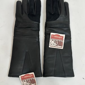 May include: A pair of black leather gloves with a long gauntlet design. The gloves have a soft, black suede patch on the back of the hand and decorative horizontal stitching. Each glove has a small tag with the text "ARDesigns".