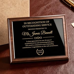 Puede incluir: Una placa de reconocimiento rectangular de madera con un panel central negro que presenta texto dorado que dice IN RECOGNITION OF OUTSTANDING SERVICE, PROUDLY PRESENTED TO Mr. James Bennell, y un logotipo circular, acompañada de una caja beige.