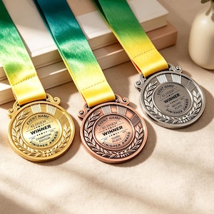 Può includere: Tre medaglie metalliche circolari con finiture oro, bronzo e argento, ciascuna attaccata a un nastro sfumato verde e giallo. Le medaglie presentano bordi a foglie di alloro e testo che include Event Name, 42.195KM, Winner e Finisher Award.