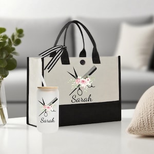 Puede incluir: Un bolso tote beige y negro y un vaso de vidrio. Ambos artículos presentan un diseño floral con tijeras y un peine, y el nombre "Sarah". El bolso tote tiene asas negras y un lazo a rayas blanco y negro.