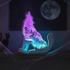 May include: A Halloween-themed display featuring a howling wolf silhouette with a mountain and forest scene illuminated in purple and blue. The scene includes carved pumpkins, candles, and a full moon backdrop.