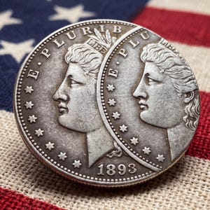May include: A silver-toned coin featuring a profile portrait of a figure wearing a headband with the word LIBERTY, surrounded by stars and the text E PLURIBUS UNUM. The coin displays the year 1893 at the bottom and has a circular metallic edge.