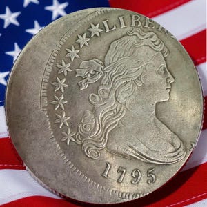Może przedstawiać: Srebrna moneta z 1795 roku, przedstawiająca profil kobiety, gwiazdy i napis "LIBERTY". Moneta spoczywa na tle amerykańskiej flagi, z czerwono-białymi pasami i niebieskim polem gwiazd.