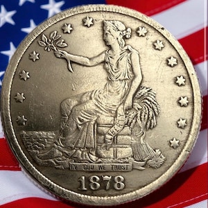 May include: A gold-colored coin featuring a seated woman holding a sprig and a banner with the word "LIBERTY". The coin is dated 1878 and inscribed with "IN GOD WE TRUST". The coin is set against an American flag.