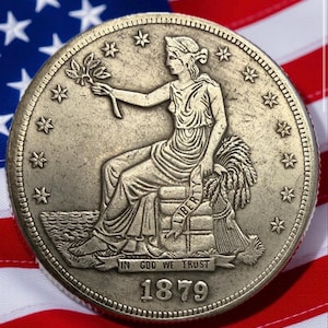 May include: A detailed image of an antique coin featuring a seated female figure holding a sprig. The coin is dated 1879 and includes the inscription "IN GOD WE TRUST." The coin is set against a backdrop of the American flag.