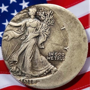 May include: A silver Walking Liberty half dollar coin, featuring a woman walking with a bundle of branches, set against a backdrop of the American flag. The coin has the inscription "IN GOD WE TRUST" and the year 1916.