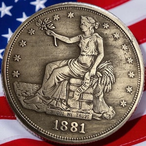 Puede incluir: Primer plano de una moneda antigua de 1881, con una mujer sentada sosteniendo una ramita y un haz de trigo. La moneda está colocada sobre un fondo de la bandera estadounidense, con sus estrellas y rayas visibles.