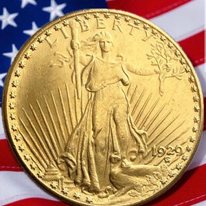 May include: A gold coin featuring a detailed relief of a woman holding a staff and a branch, with the year 1929. The coin is set against the backdrop of the American flag, with its red and white stripes and blue field of stars.