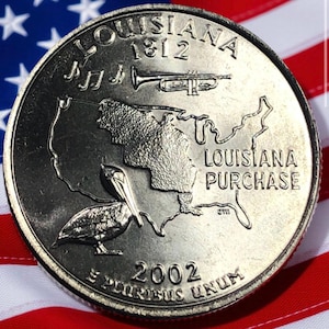 May include: A close-up of a 2002 Louisiana state quarter coin. The coin features a pelican, musical notes, a trumpet, and a map of Louisiana. The coin is set against a backdrop of the American flag.