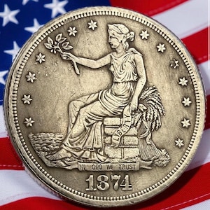 May include: A silver coin from 1874 featuring a seated woman holding a sprig and wheat. The coin is set against an American flag background. The coin's inscription reads "IN GOD WE TRUST" and "LIBERTY".
