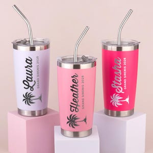 May include: Three stainless steel tumblers in pastel colors: lavender, pink, and hot pink. Each tumbler has a silver lid and straw. The names "Laura", "Heather", and "Stasha" are printed on the tumblers, along with a palm tree graphic and the text "GRAND SIRENIS 2025".