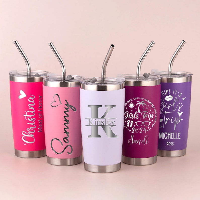 May include: Five stainless steel tumblers with lids and straws. Each tumbler is a different color: pink, light pink, white, dark pink, and purple. The tumblers have personalized text, including names and phrases like "Girls Trip."