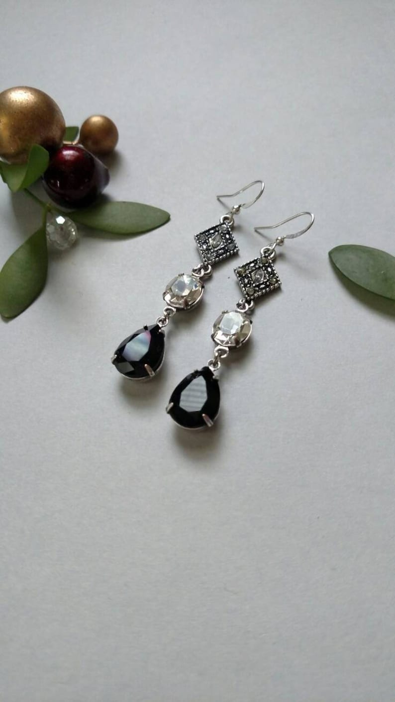 Pu&ograve; includere: Un paio di orecchini pendenti in argento con cristalli neri e trasparenti a forma di goccia e cristalli quadrati con accenti argentati.