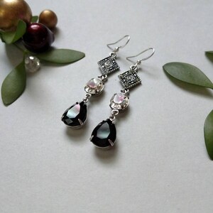 Pu&ograve; includere: Un paio di orecchini pendenti in argento con pietre a forma di lacrima nere e iridescenti e pietre quadrate con strass trasparenti.