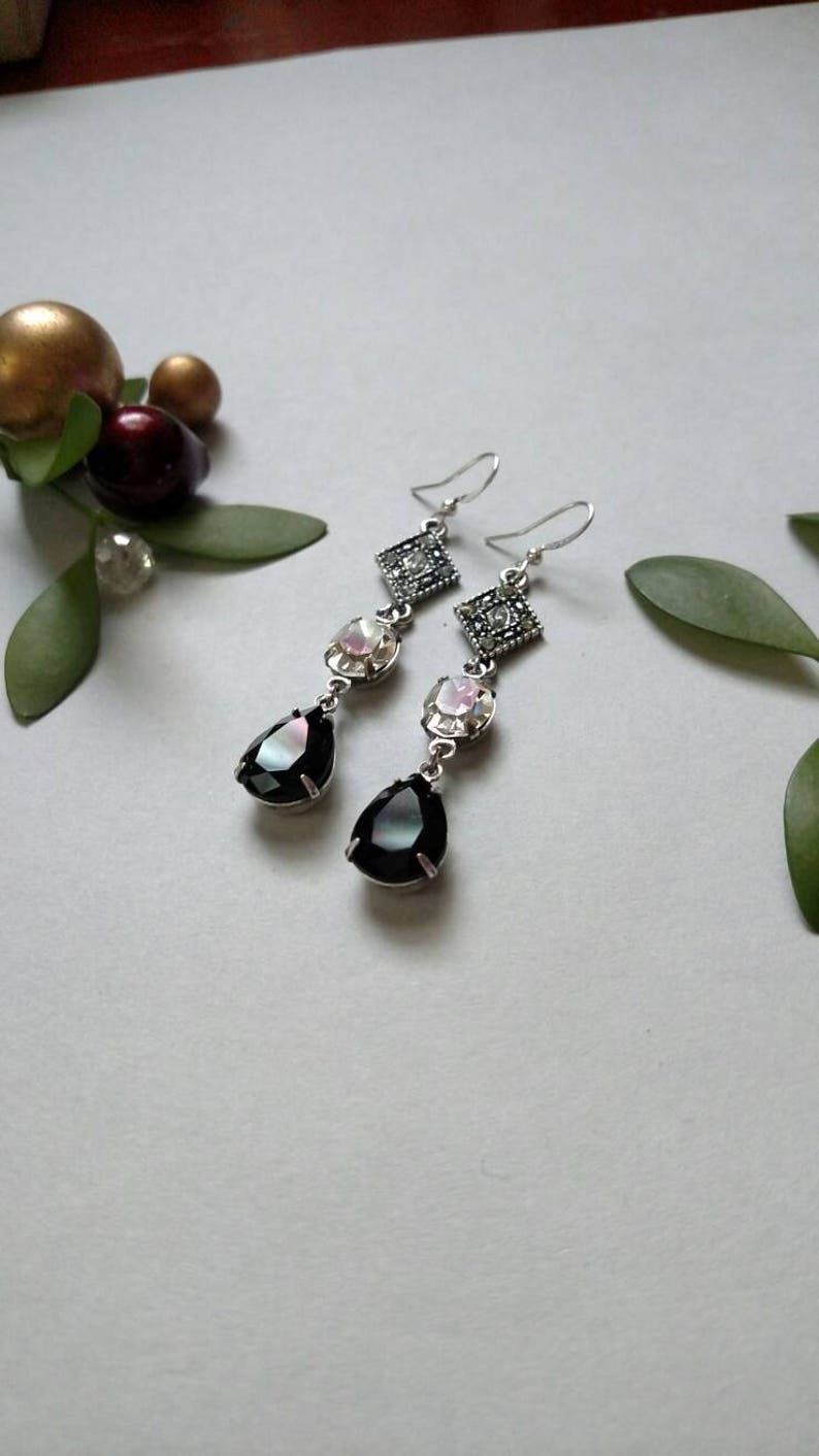 Pu&ograve; includere: Un paio di orecchini pendenti in argento con pietre a forma di lacrima nere e iridescenti e pietre quadrate con strass trasparenti.