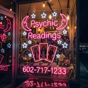 May include: A neon sign in a window displaying the text Psychic Readings and the phone number 602-717-1233. The sign features pink crescent moons, white stars, and three illuminated tarot card graphics, all set against a dark storefront background.