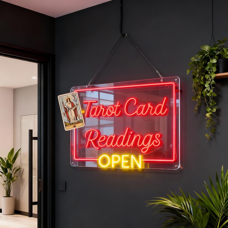 May include: A rectangular neon sign with a clear acrylic backing, featuring the red text "Tarot Card Readings" and the yellow text "OPEN". A single tarot card depicting a figure is attached to the left side. The sign hangs by black wires.