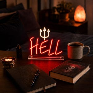 Op de afbeelding: Een rood neonbord met het woord HELL in een cursief lettertype, met een wit neon-drietandsymbool boven de tekst. Het bord is gemonteerd op een doorzichtige rechthoekige acrylvoet en straalt een heldere rode gloed uit op het oppervlak.