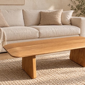 Op de afbeelding: Een lage salontafel gemaakt van lichtgekleurd hout, met een glad, rechthoekig tafelblad met afgeronde randen en twee stevige, verticale, plaatvormige poten die een stabiele basis vormen voor dit functionele meubelstuk.