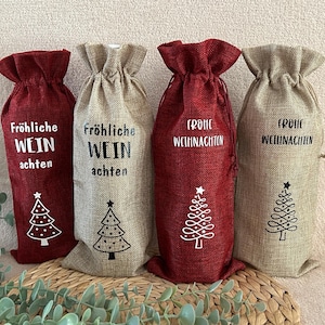 Könnte beinhalten: Vier Weinflaschenbeutel aus rotem und beigem Jute. Jeder Beutel hat einen Kordelzugverschluss und ein weißes oder schwarzes Weihnachtsbaumdesign. Der Text auf Deutsch lautet "Fröhliche Wein achten" und "Frohe Weihnachten".