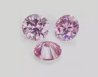 Puede incluir: Tres piedras preciosas rosas redondas y facetadas dispuestas en formación triangular. Cada piedra presenta un corte brillante con numerosas facetas triangulares que reflejan la luz, creando un aspecto brillante con tonos de rosa.