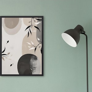 Puede incluir: Impresión artística abstracta en un marco negro. La obra presenta formas beige y negras con elementos botánicos. A la derecha de la obra enmarcada hay una lámpara de pie negra con interior blanco. La pared es de color verde apagado.