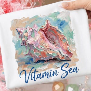 Peut inclure: Un t-shirt blanc avec un motif carré représentant un coquillage peint à l'huile dans des tons rose, pêche, bleu et vert. Sous le coquillage, le texte Vitamin Sea est imprimé en bleu foncé avec une police cursive sur le tissu blanc.