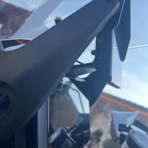 May include: Close-up of a motorcycle's windshield and fairing. The fairing is black and angular, with a clear windshield. The image is taken from a low angle, showing the details of the motorcycle's front.
