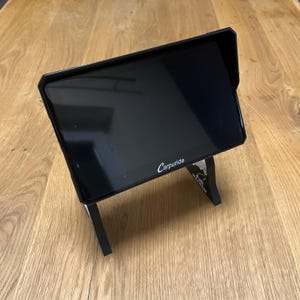 May include: A black tablet with a sun visor is displayed on a black stand. The tablet screen is blank. The word "Carpuride" is printed in white on the lower right corner of the screen.