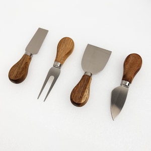 Könnte beinhalten: Ein Set aus vier Käsemessern mit Edelstahlklingen und Holzgriffen. Das Set enthält ein flaches Messer, eine Gabel und zwei verschiedene Klingenformen. Die Griffe sind braun.