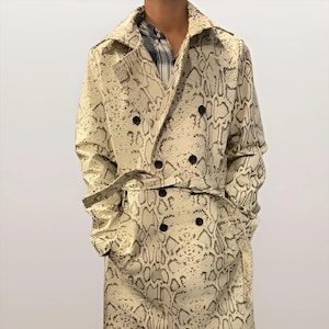 May include: A long, double-breasted trench coat with a snakeskin pattern in cream and dark brown. The coat features a belt, large lapels, and black buttons. The coat's length is approximately 50 inches.