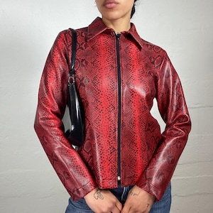 May include: A long-sleeved jacket featuring a vibrant red and black snakeskin pattern, a pointed collar, and a central black zipper closure. The jacket is paired with a smooth black shoulder bag and blue denim jeans, creating a distinct look.