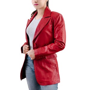 May include: A vibrant red leather blazer with a classic notched lapel and a single-button closure. The blazer features a tailored fit, a chest pocket, and two front pockets. The sleeves are long, and the blazer is worn over a gray t-shirt and blue jeans.