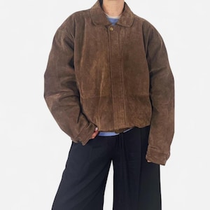 以下が含まれることがあります： 襟付き、シングルボタン留めの茶色のスエードジャケット。 クラシックでヴィンテージなスタイルで、少しオーバーサイズのフィット感です。 ジャケットはミディアムブラウン色です。