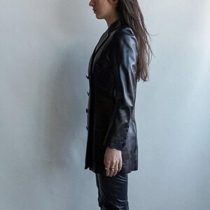 May include: A black leather blazer with a classic lapel collar and button closure. The longline jacket features long sleeves and a tailored fit. The blazer is paired with matching black leather pants. A stylish, timeless outerwear piece.