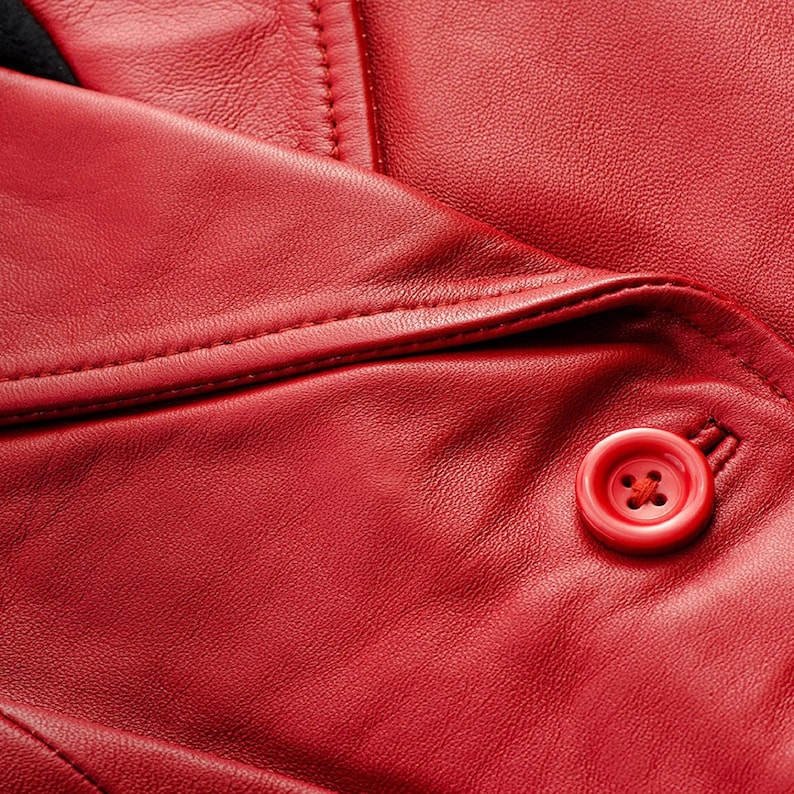 May include: Close-up of a red leather jacket, showcasing the texture and stitching details. A red button is visible, adding a pop of color. The jacket's design suggests a classic style, suitable for various occasions.
